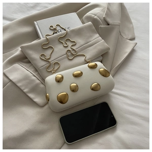 Détail du sac boîte crème avec décorations dorées sur une veste de costume beige