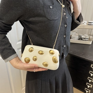 Pochette boîte blanche avec clous ovales dorés et bandoulière chaîne portée par un mannequin