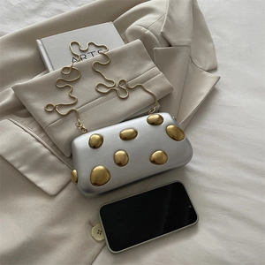 Pochette boîte argent mat avec clous dorés et fine chaîne sur un blazer blanc