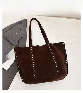 Detail of dark brown suede tote bag featuring silver rivet studs on a white background