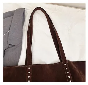 Detail of dark brown suede tote bag featuring silver rivet accents and comfortable dual straps