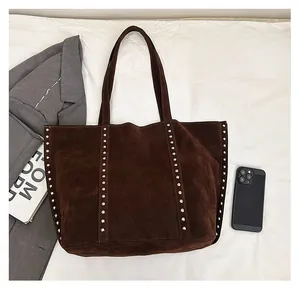 Top-down view of large brown suede tote with rivet details and daily items for scale