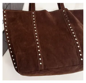 Detail of dark brown suede tote bag featuring silver rivet studs and textured fabric