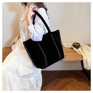Detailed view of black suede tote bag with silver studs worn on shoulder by model