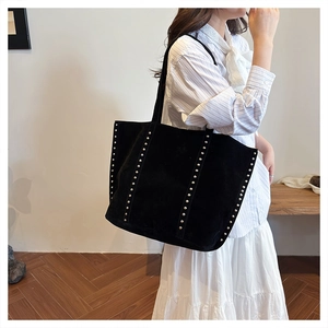 Detailed view of black suede tote bag featuring vertical silver rivet studs and long straps