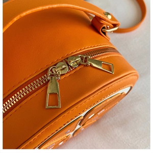 Close-up of bright orange lemon crossbody bag featuring double gold zippers and PU leather texture