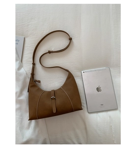 Detail of brown pebbled leather shoulder bag with white stitching next to a tablet