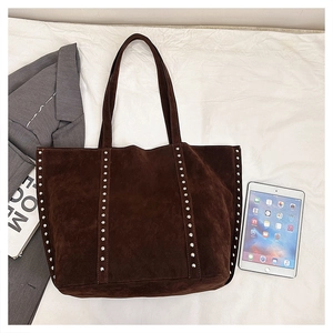 Flat lay of dark brown suede tote bag with silver rivets next to an iPad for size