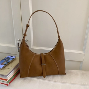 Brown leather hobo bag with white contrast stitching and silver buckle on white table