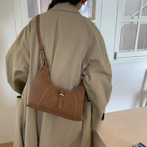 Detail of brown leather baguette bag with contrast stitching and silver buckle on model