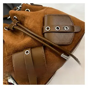Macro shot of brown suede bucket bag featuring leather pocket and silver metal eyelets