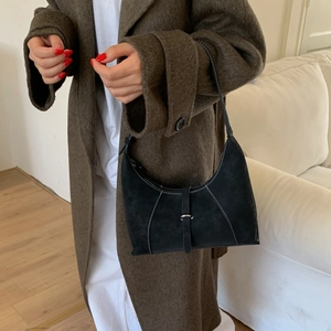 Detail of black suede underarm bag with white contrast stitching on wool coat