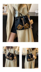 Detail of black drawstring bucket bag with brown leather trim and cute teddy bear charm