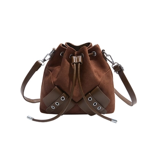 Close-up of brown suede drawstring bucket bag with metal ring rivets and faux leather trim