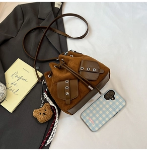 Detail of brown suede bucket bag featuring front pockets and cute plush bear charm accessory