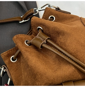 Detail of brown faux suede bucket bag featuring drawstring closure and silver hardware