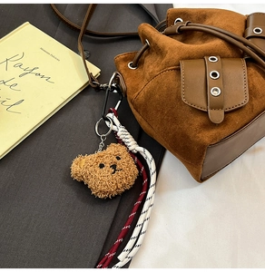 Suede drawstring bucket bag detail with plush bear charm and vintage metal buckle