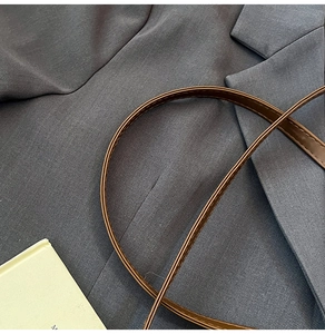 Close-up of brown PU leather shoulder strap with fine stitching on a grey blazer