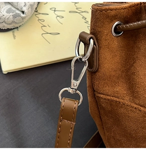 Detailed macro view of silver metal hook hardware and neat stitching on brown suede bag