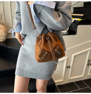 Detail of a brown suede drawstring bucket bag with silver eyelets and adjustable strap