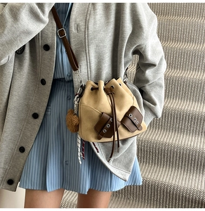 Detail of drawstring bucket bag with brown leather pockets and plush charm on staircase