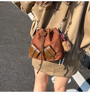 Detail of brown suede bucket bag with drawstring closure and cute bear charm accent