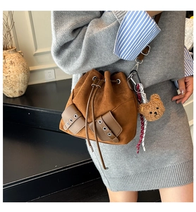 Brown faux suede drawstring bucket bag with decorative front pockets and bear charm