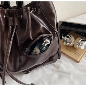 Detailed view of high-gloss dark brown leather bucket bag with drawstring and side pocket