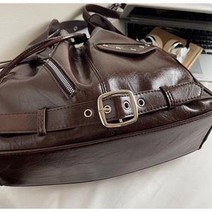 Close-up of brown glossy faux leather tote featuring metallic studs and motor hardware details