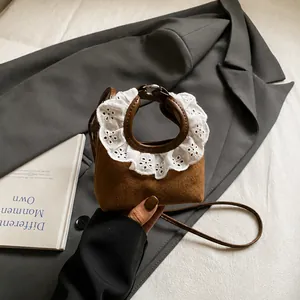 Detailed view of mini brown suede crossbody bag featuring white lace ruffle handles