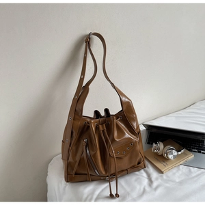 Detail of caramel brown faux leather bucket bag with silver studs and long zipper pulls