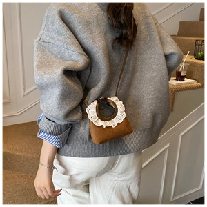 Close-up of mini brown suede crossbody bag with white lace trim worn with casual grey sweater