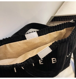 Close-up of black corduroy tote bag with embroidered letters and magnetic closure