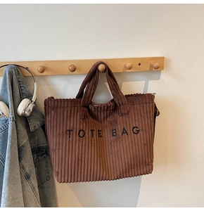 Detailed view of brown corduroy tote bag with embroidered letters on a wall hook