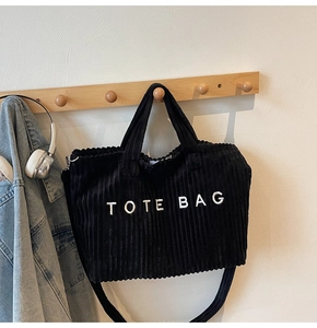 Detail of black corduroy tote bag with white TOTE BAG embroidery and adjustable strap