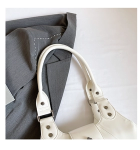 Close-up of white leather underarm bag featuring silver rivets and metal buckle detail