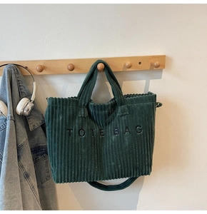 Detail of dark green corduroy tote bag with embroidered letters and adjustable strap