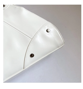 Close-up of white leather handbag featuring dark metal rivets and precise double stitching