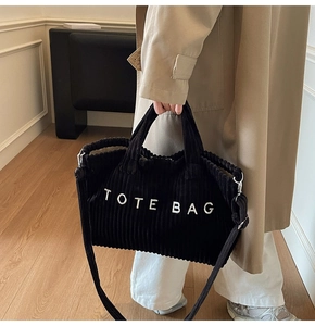 Detail of black corduroy tote bag texture and white lettering with silver metal buckles