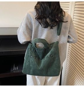 Detail of dark green corduroy tote bag showing metal buckles and texture on a model