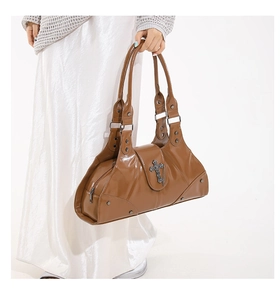 Close-up of brown patent leather handbag with vintage metal cross and chain details