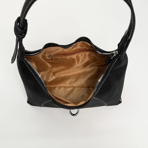 Minimalist black baguette shoulder bag with white stitching and tan fabric interior