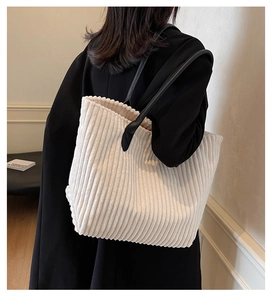 Detail of off-white corduroy tote bag with black leather straps on a model