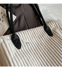 Detail of off-white corduroy tote bag showing textured fabric and black leather handles