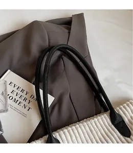 Close-up of white corduroy tote bag featuring black leather handles and reinforced stitching