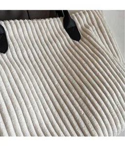 Close-up of off-white corduroy tote bag featuring thick ribbed texture and black faux leather handle