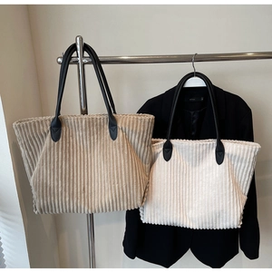 Detailed close-up of corduroy tote bags in beige and white with black leather handles