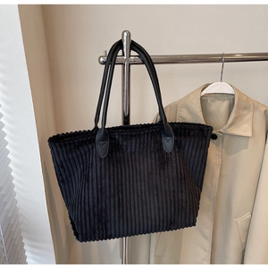 Detail of black corduroy tote bag with leather straps on a metal hanger