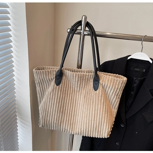 Detail of beige corduroy tote bag with vertical texture and black leather handles