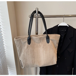 Detail of corduroy tote bag showing vertical rib texture and black leather handles